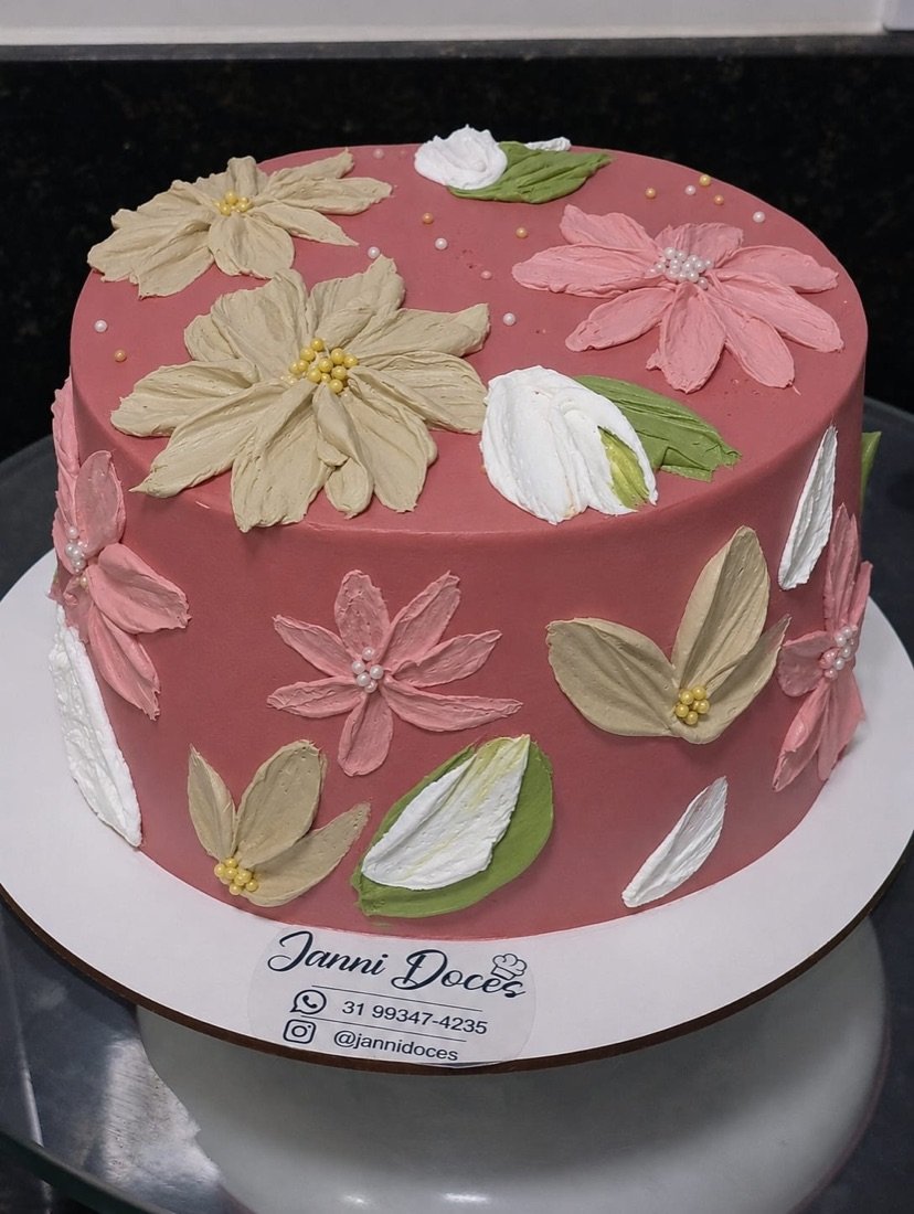 Bolo rosa decorado com flores de chantininho, com a etiqueta Janni Doces